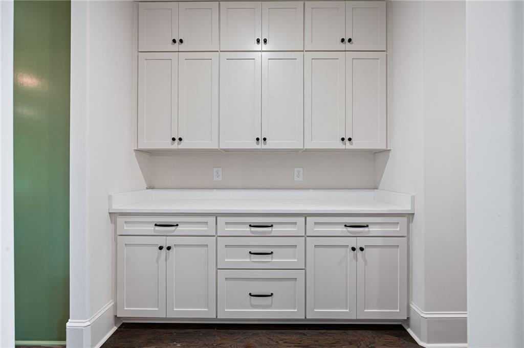 Built-in white cabinets and counter with dark pulls, beside a green wall.