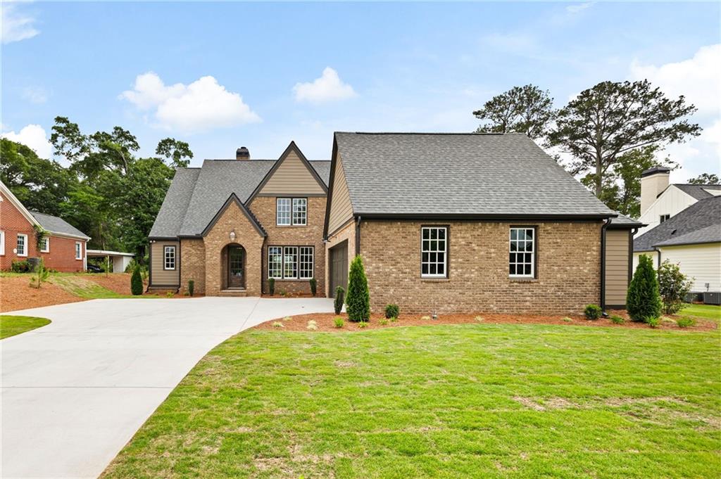Brick house with steep gabled roofs, a broad driveway, and a green front lawn.