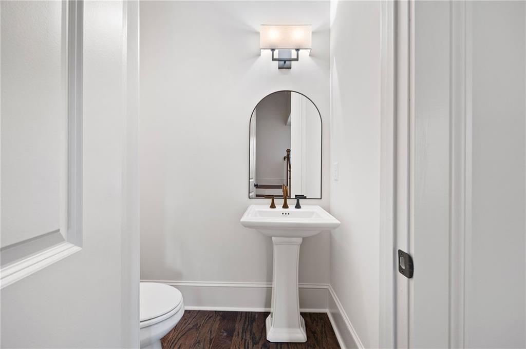 Bathroom with a white pedestal sink, arched mirror, and dark wood flooring.