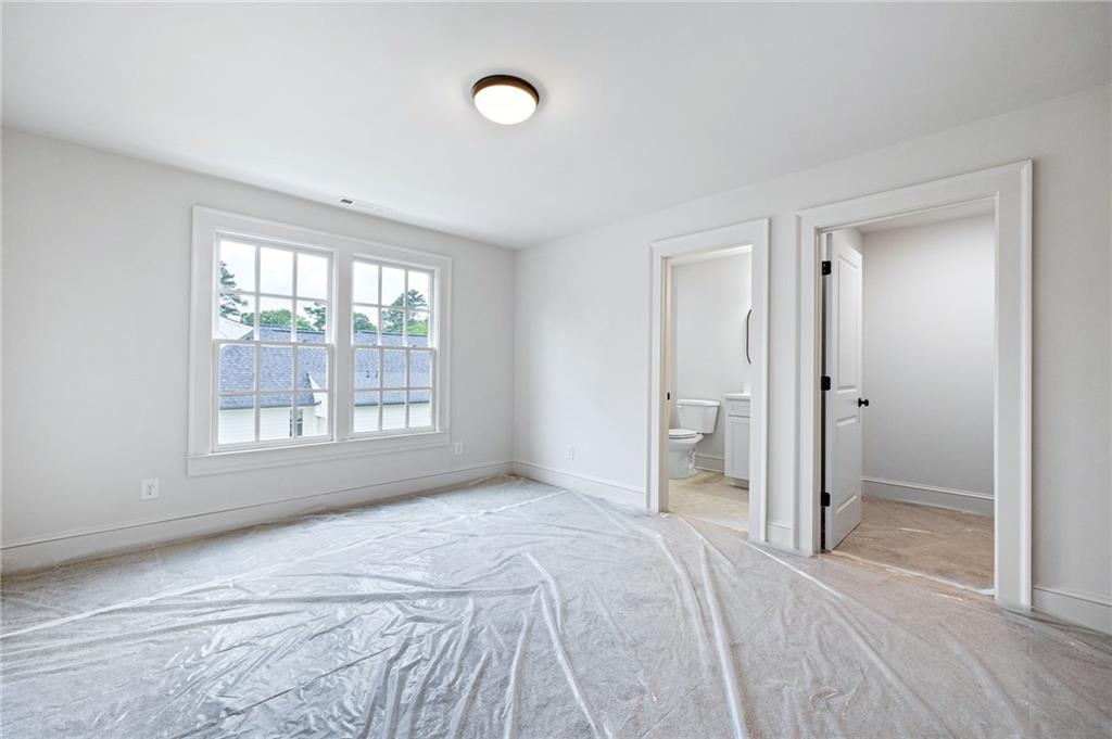 Empty bedroom with a large window, floor covered in protective plastic, and an adjoining bathroom.