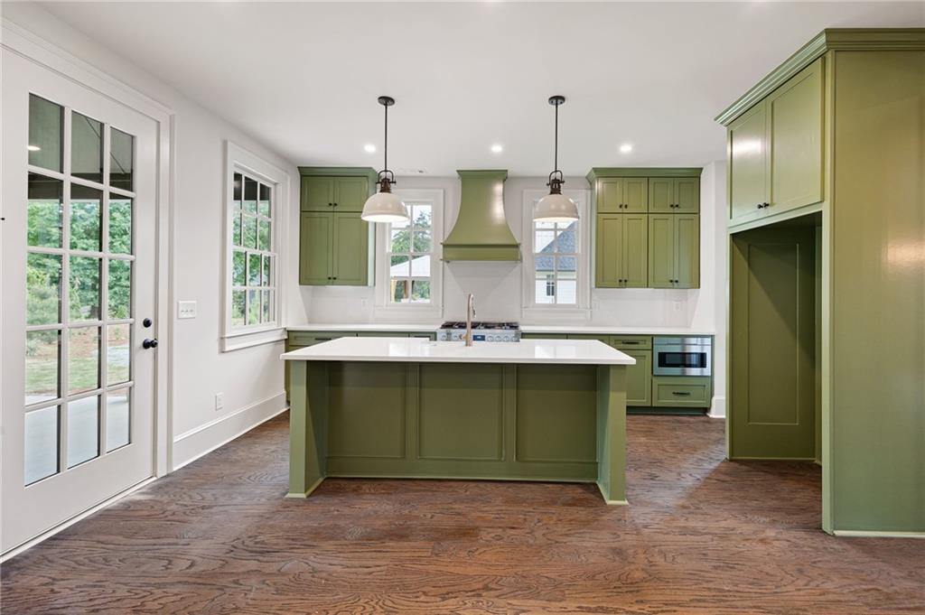Kitchen with sage-green cabinets, a large white island, pendant lights, and wood flooring.
