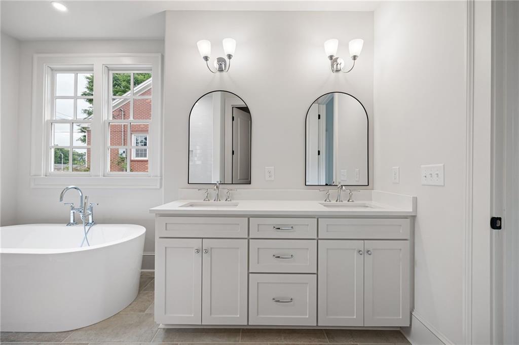 Bathroom with a double-sink vanity and freestanding tub beside a large window.
