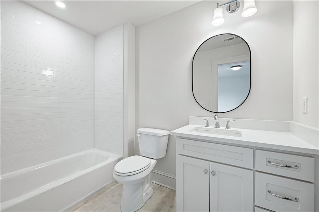 Bathroom with a white subway-tile tub surround, toilet, and vanity beneath an oval mirror.