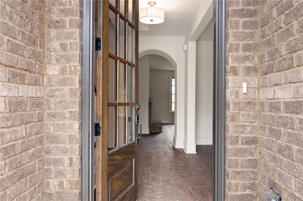 Open wood-and-glass front door reveals a bright foyer with dark hardwood floors and an arched opening.