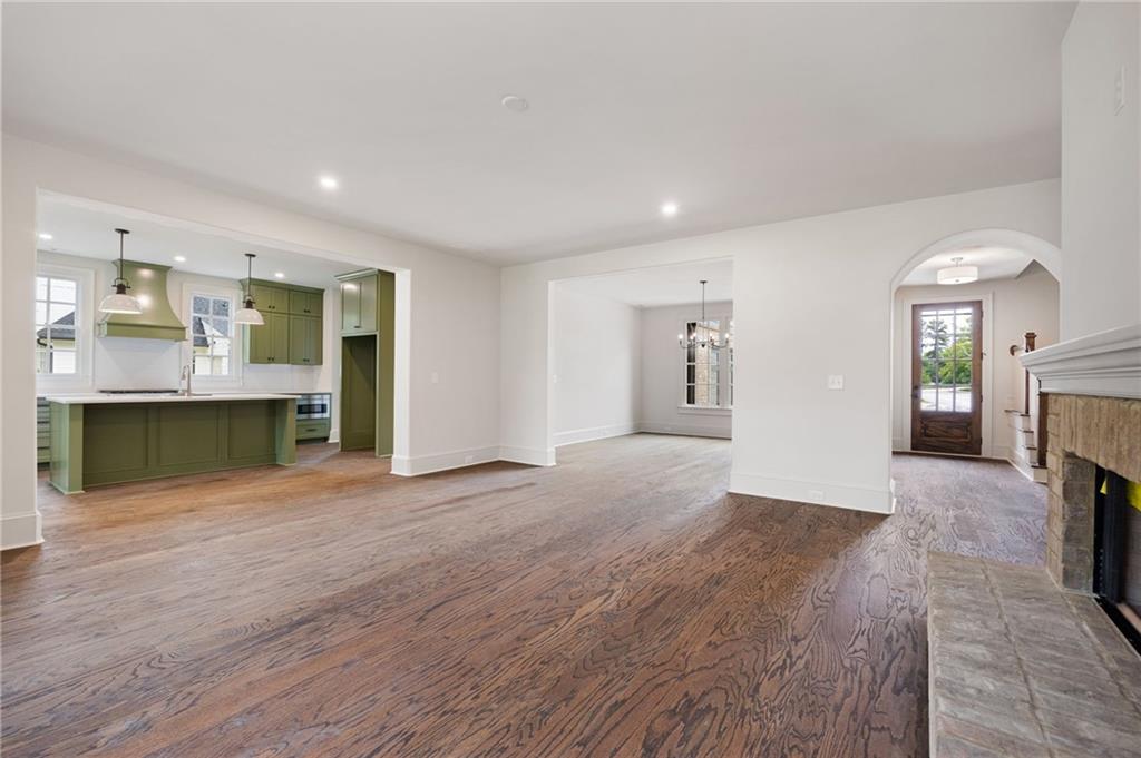 Open living room with hardwood floors, sage-green kitchen cabinets, and a stone fireplace.