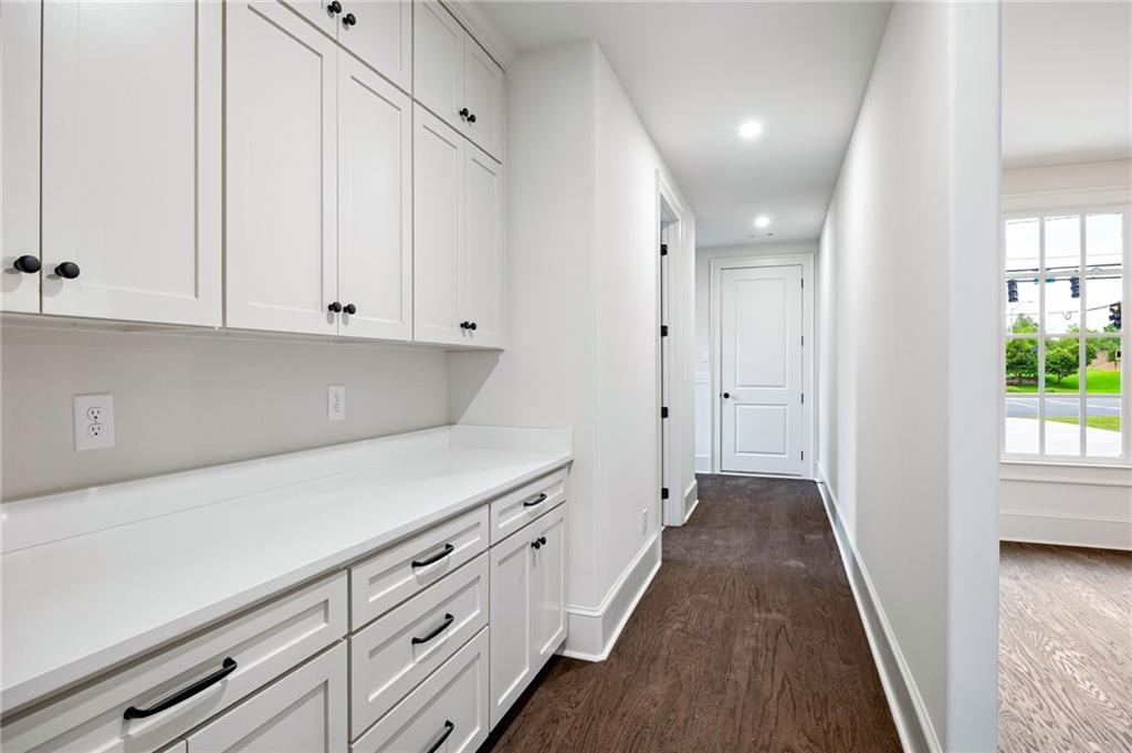 Bright hallway with white built-in cabinets and countertop, dark wood floors, and a window overlooking greenery.