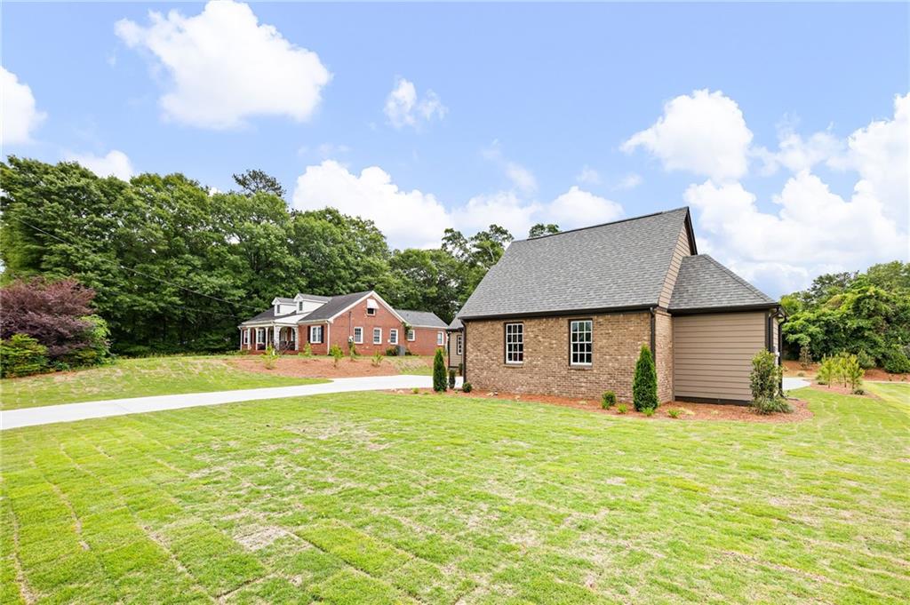 Brick house and separate outbuilding beside a broad lawn and paved driveway.
