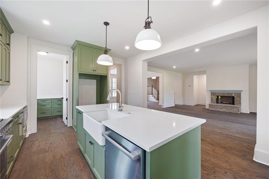 Open kitchen with sage-green cabinets, white island, farmhouse sink, and adjoining living room with stone fireplace.