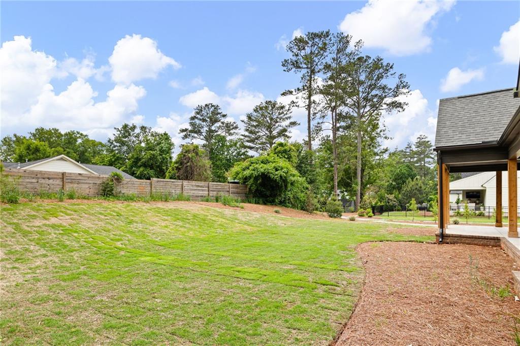 Backyard with a broad lawn, wooden privacy fence, mature trees, and a covered patio.