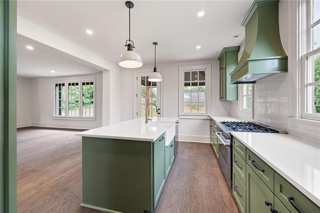 Kitchen with green cabinets, a large white island, and a gas range beneath a green hood.