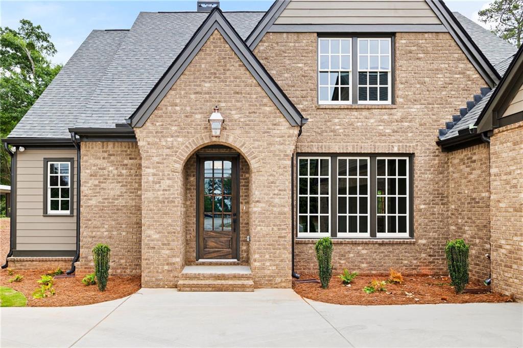 Brick-front home with an arched wood entry, steep gables, and a broad concrete driveway.