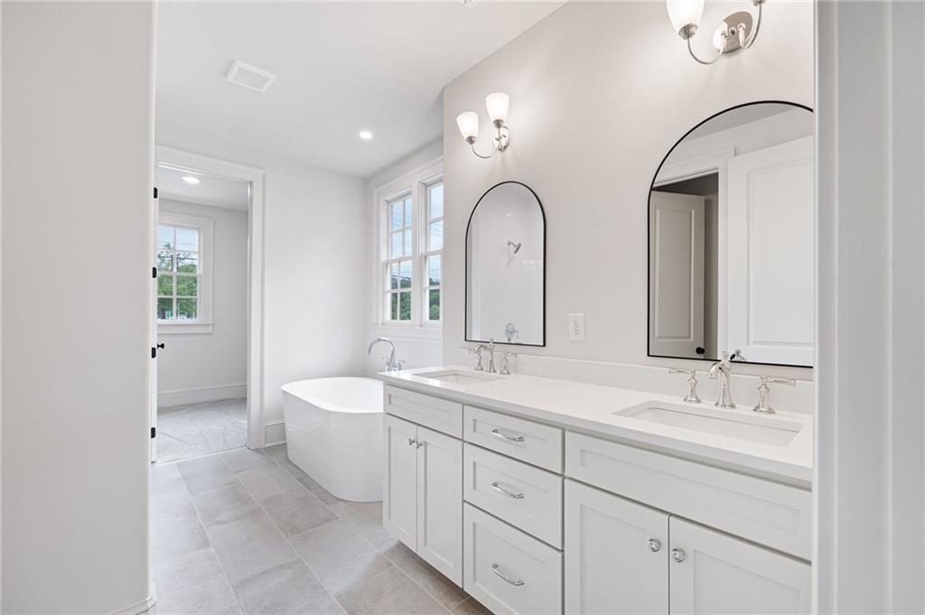 Bright bathroom with a double vanity, arched mirrors, and a freestanding soaking tub.