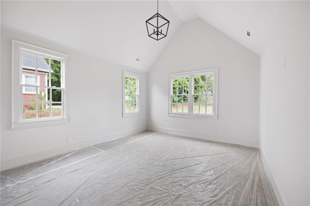 Bright empty room with a vaulted ceiling, three windows, and protective plastic covering the floor.