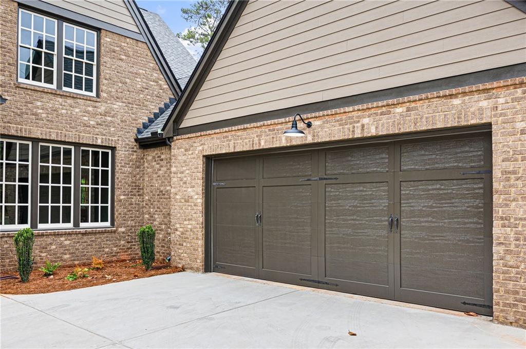 Brick house exterior with a wide dark garage door, white-trimmed windows, and concrete driveway.