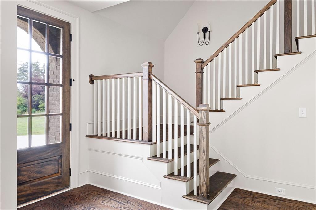 Entry foyer with a wood-and-glass front door and a staircase with white balusters and wood rails.