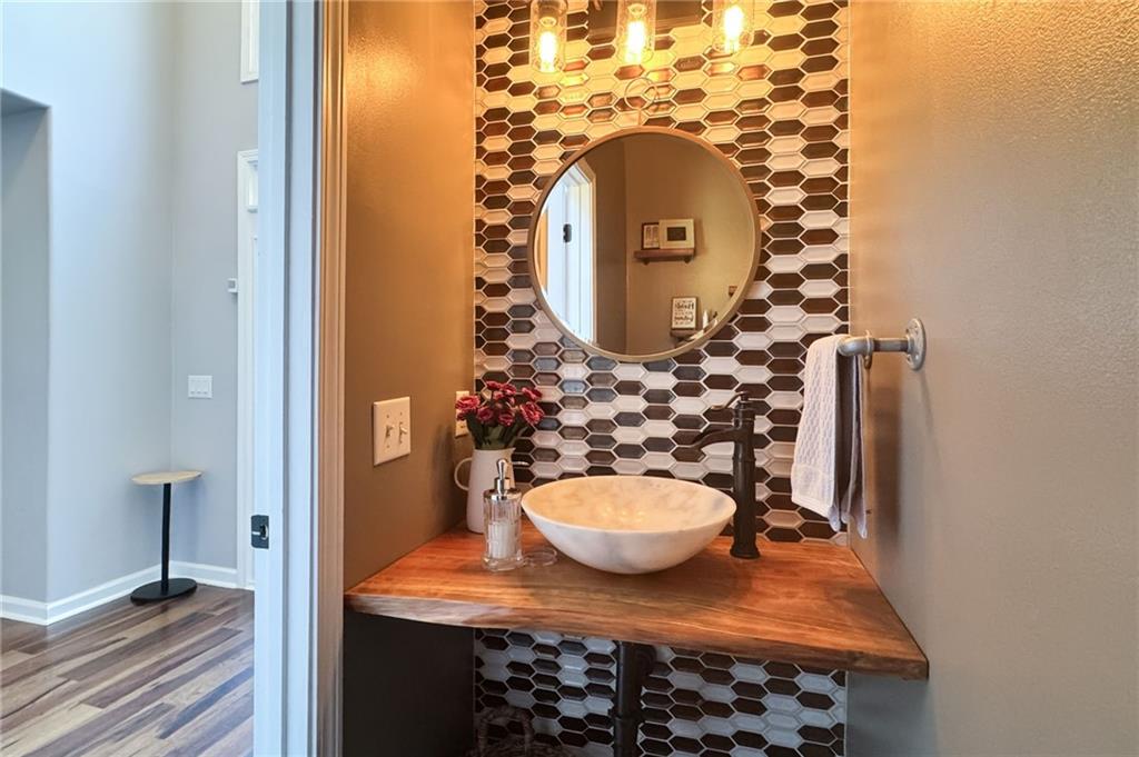Bathroom vanity with a wood countertop, vessel sink, round mirror, and hexagonal tile backsplash.