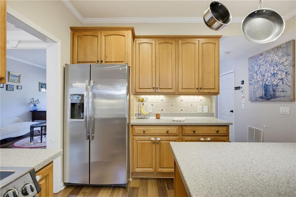 Kitchen with honey-colored cabinets, stainless steel refrigerator, and light stone countertops.