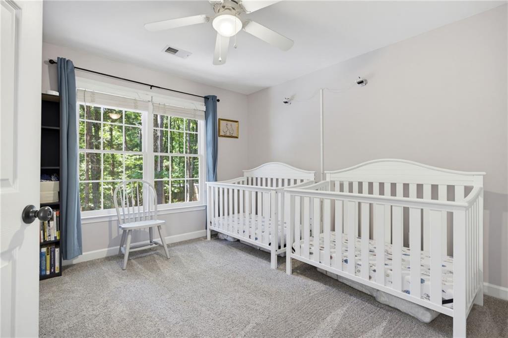 Nursery with two white cribs beside a large window overlooking trees.