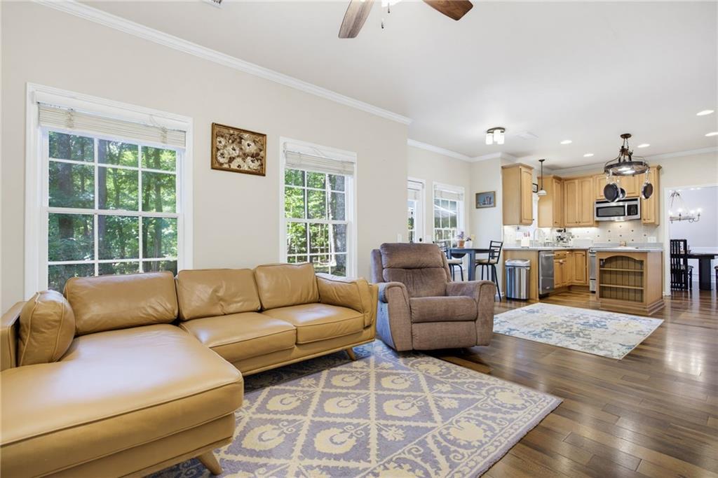 Living room with tan leather sectional and recliner beside an open kitchen with light wood cabinets.