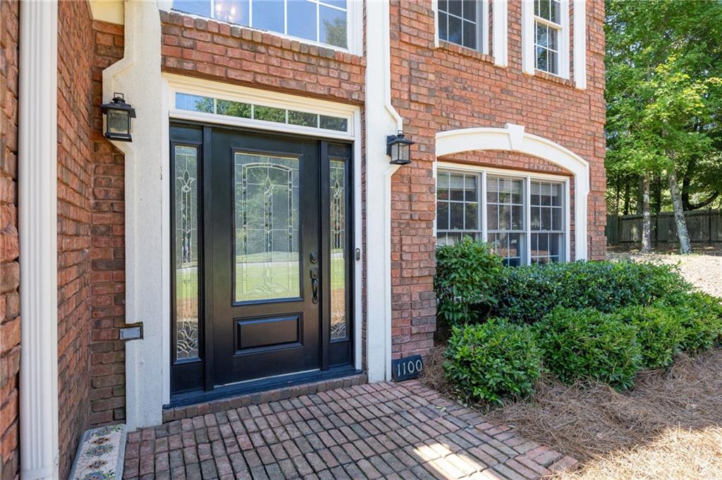 Brick home entrance with black decorative-glass doors, white trim, and a brick walkway.