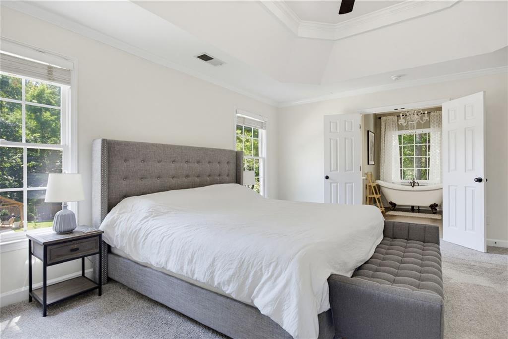 Primary bedroom with a gray upholstered bed and open doors to a bathroom with a freestanding tub.