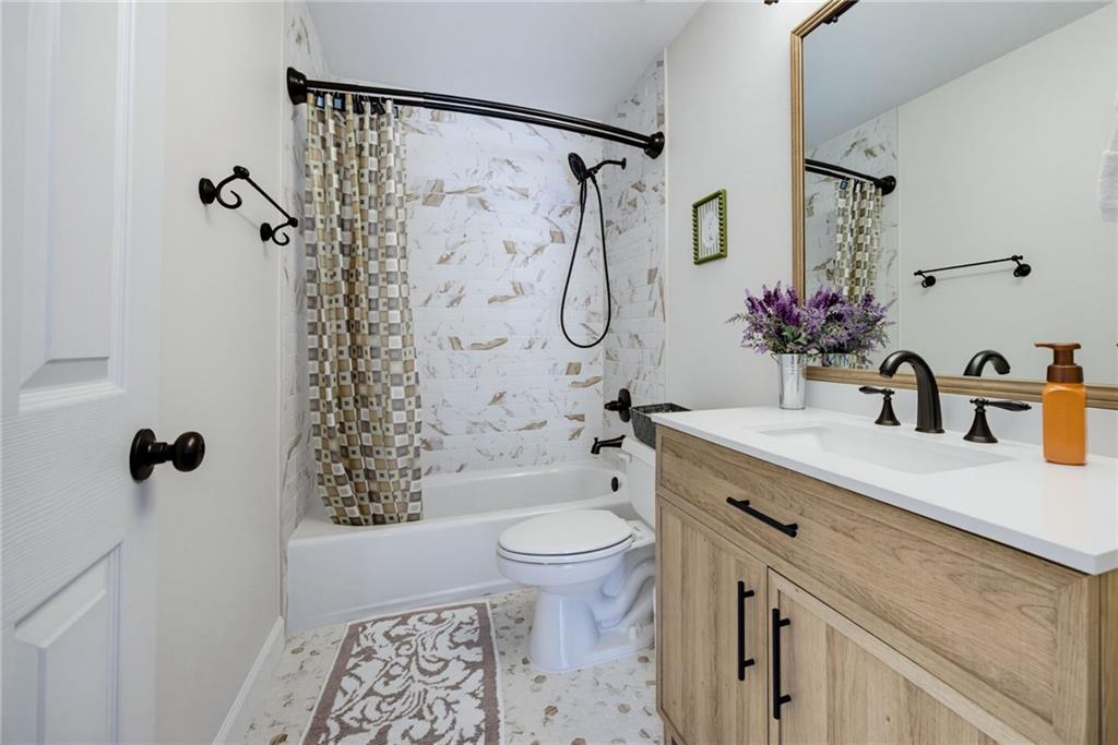 Bathroom with marble-look tub surround and a light wood vanity with black fixtures.