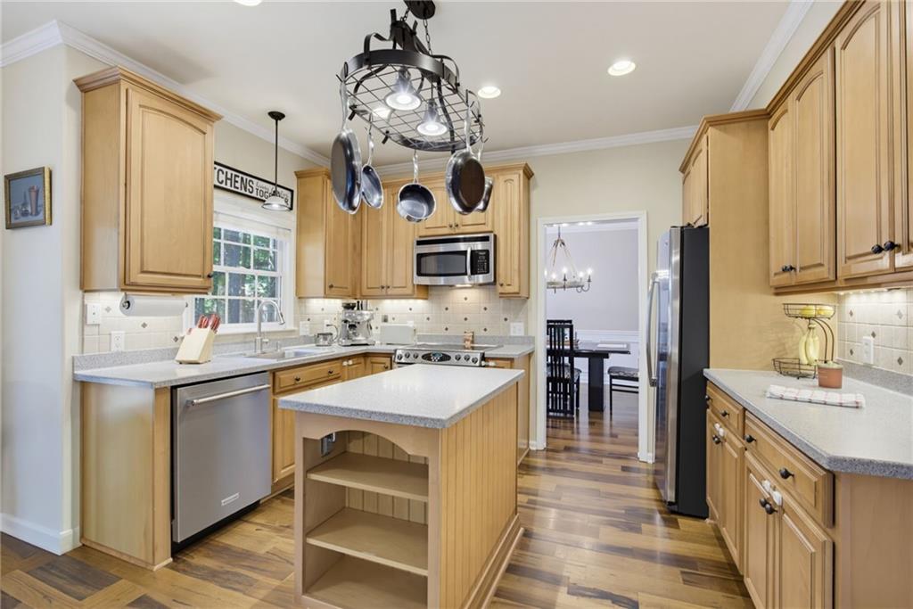 Kitchen with honey-toned cabinets, stainless steel appliances, and a central island beneath a hanging pot rack.