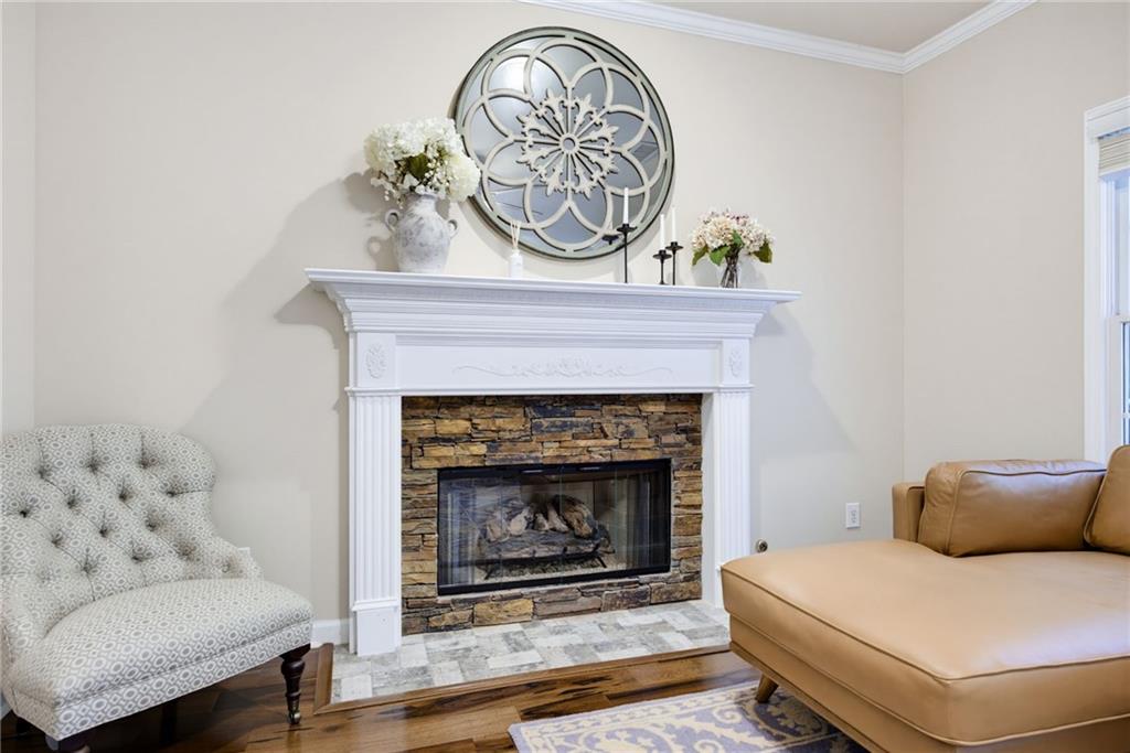 Living room with a stone-and-white fireplace, patterned armchair, and tan leather sofa.