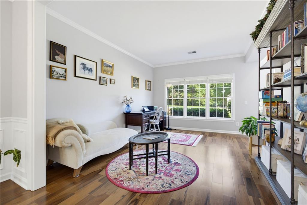 Furnished study with a cream sofa, desk, book shelving, and large windows overlooking greenery.