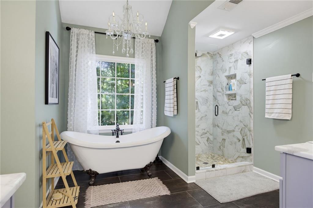 Bathroom with a clawfoot tub beneath a curtained window and a marble-look glass shower.