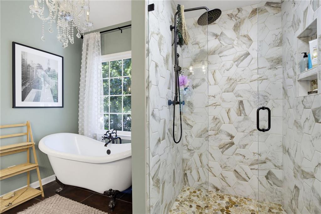 Bathroom with a clawfoot tub, crystal chandelier, and veined-tile walk-in shower.