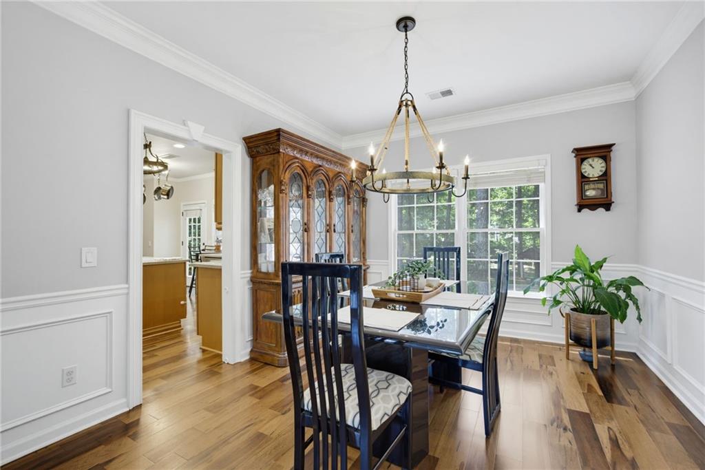 Dining room with an ornate china cabinet, chandelier, hardwood floors, and large windows overlooking greenery.