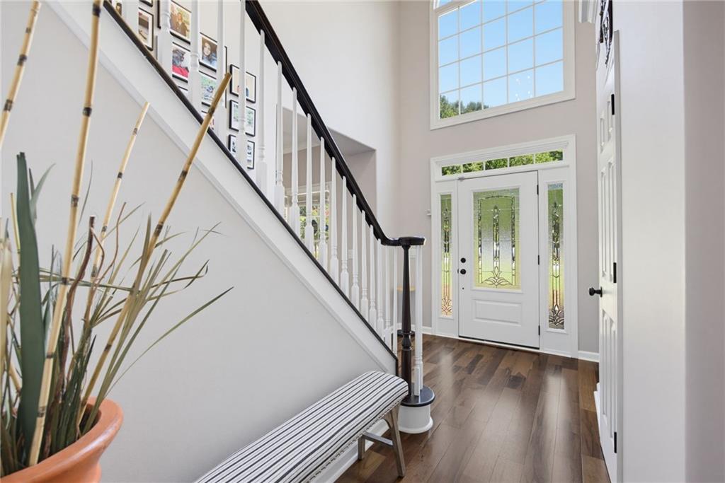 Entry foyer with a dark-railed staircase, decorative glass front door, and striped bench.