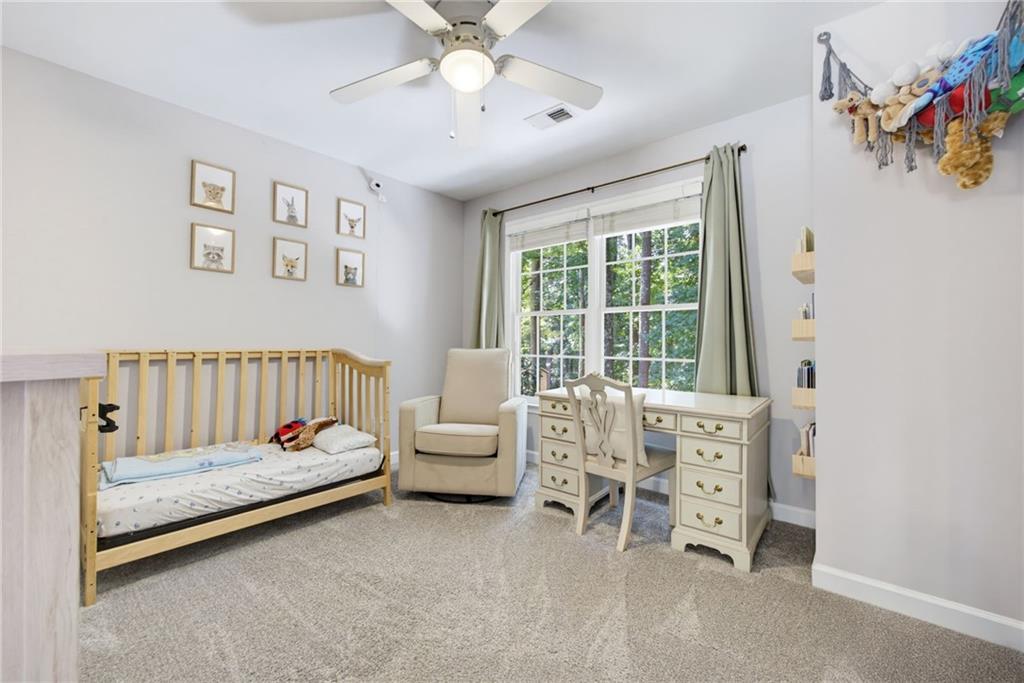 Nursery with a wooden crib, armchair, and desk beside a large window.