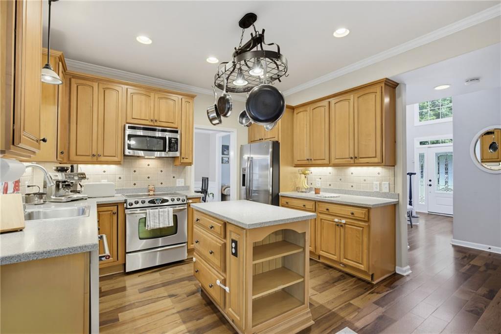 Kitchen with honey-colored cabinets, stainless steel appliances, and a central island beneath a hanging pot rack.
