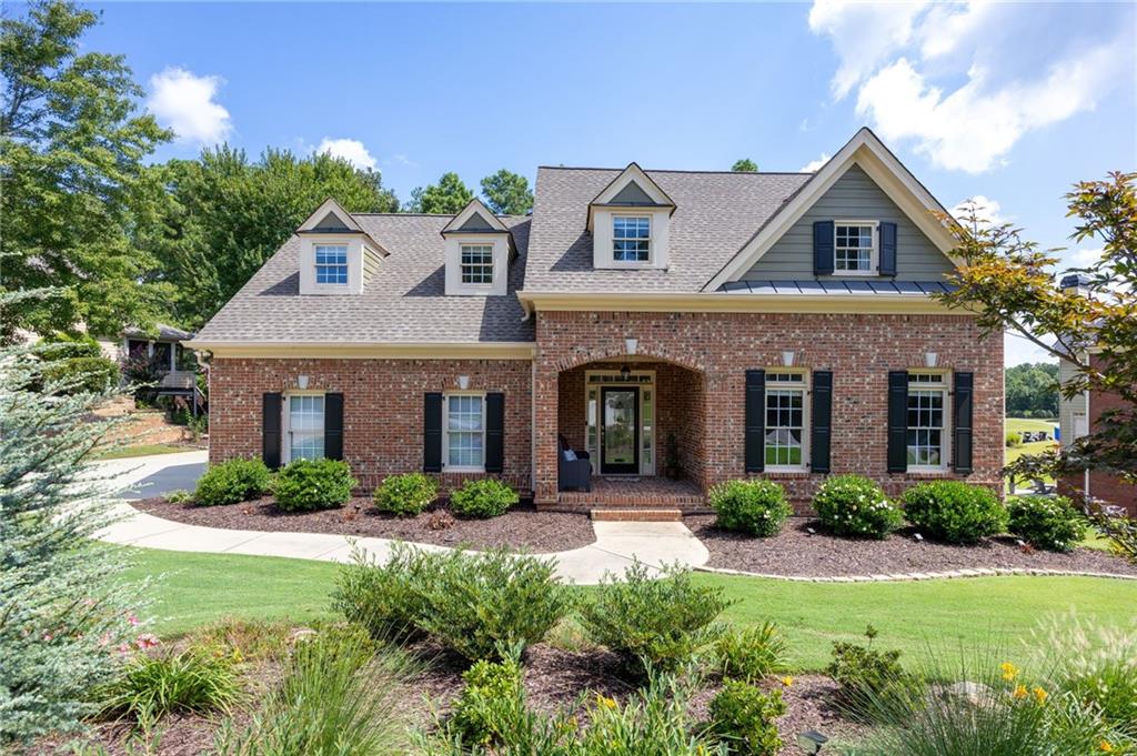 Brick home with dormers, black shutters, an arched entry, and landscaped front lawn.