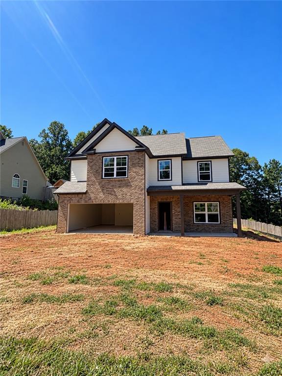 Two-story brick and siding house with an open garage and a wide, bare yard.