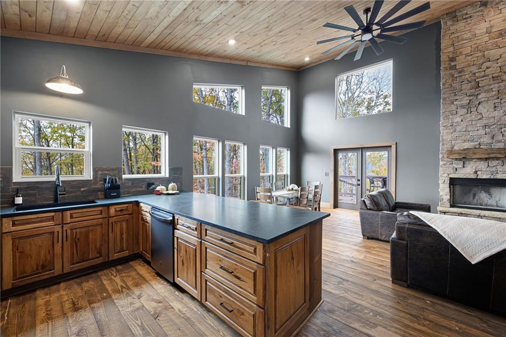 Open kitchen with a large wood island, vaulted ceiling, tall windows, and stone fireplace.