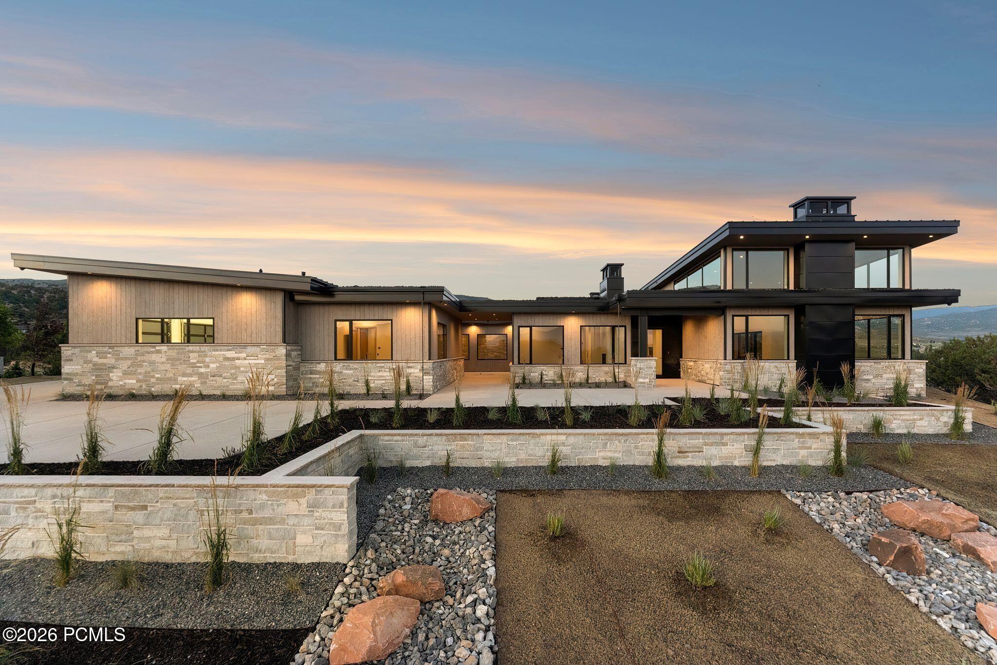 Modern home with broad windows, pale stone walls, and landscaped rock beds at dusk.