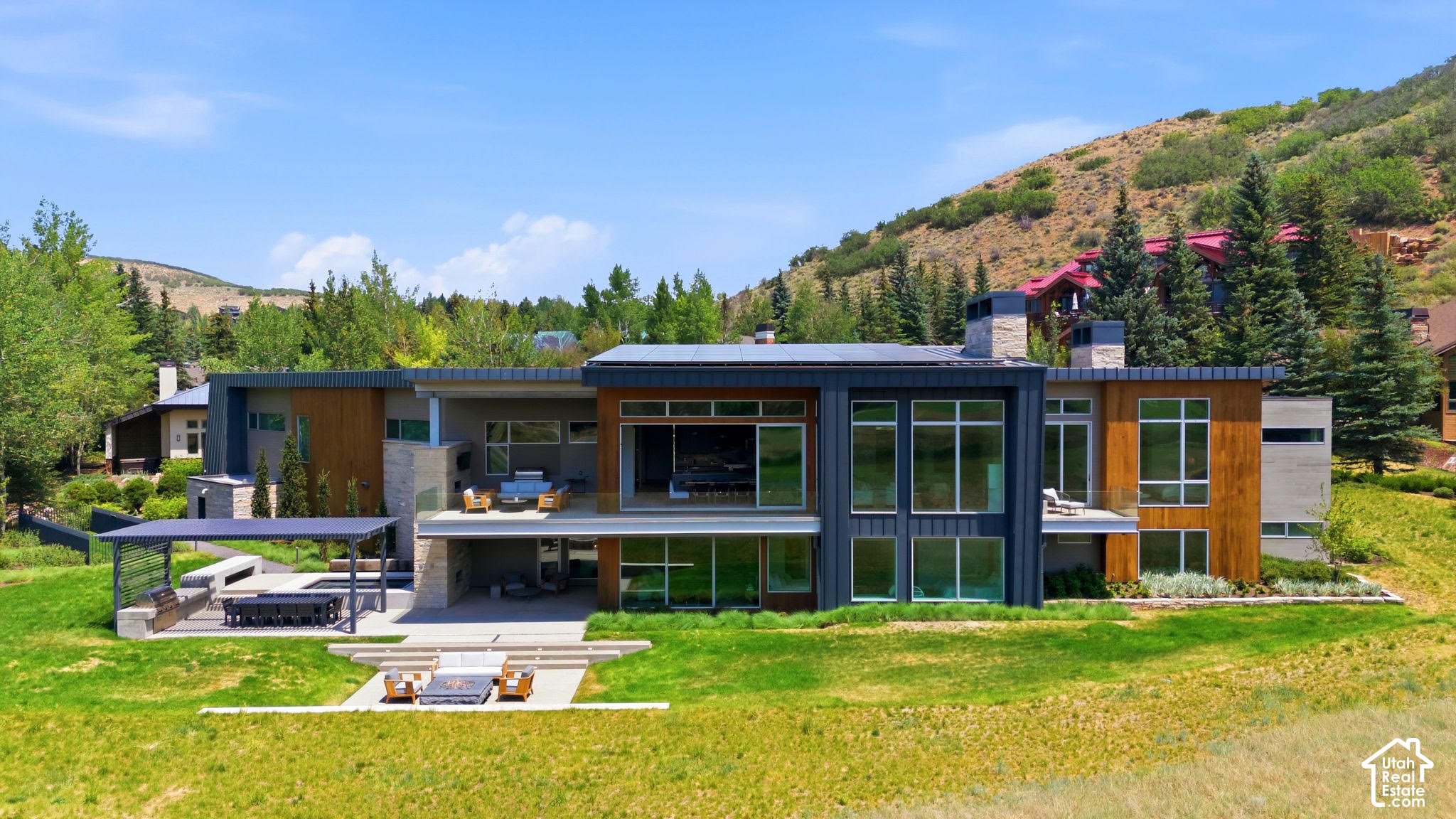 Modern hillside home with broad windows, rooftop solar panels, and outdoor seating areas.