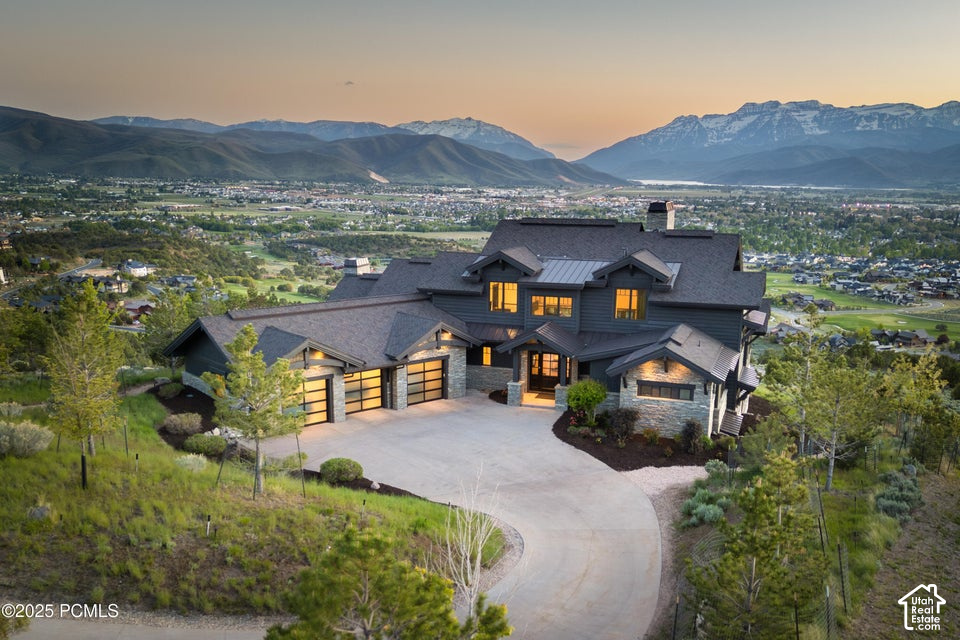Mountain home with stone accents and a curved driveway overlooking a valley at sunset.