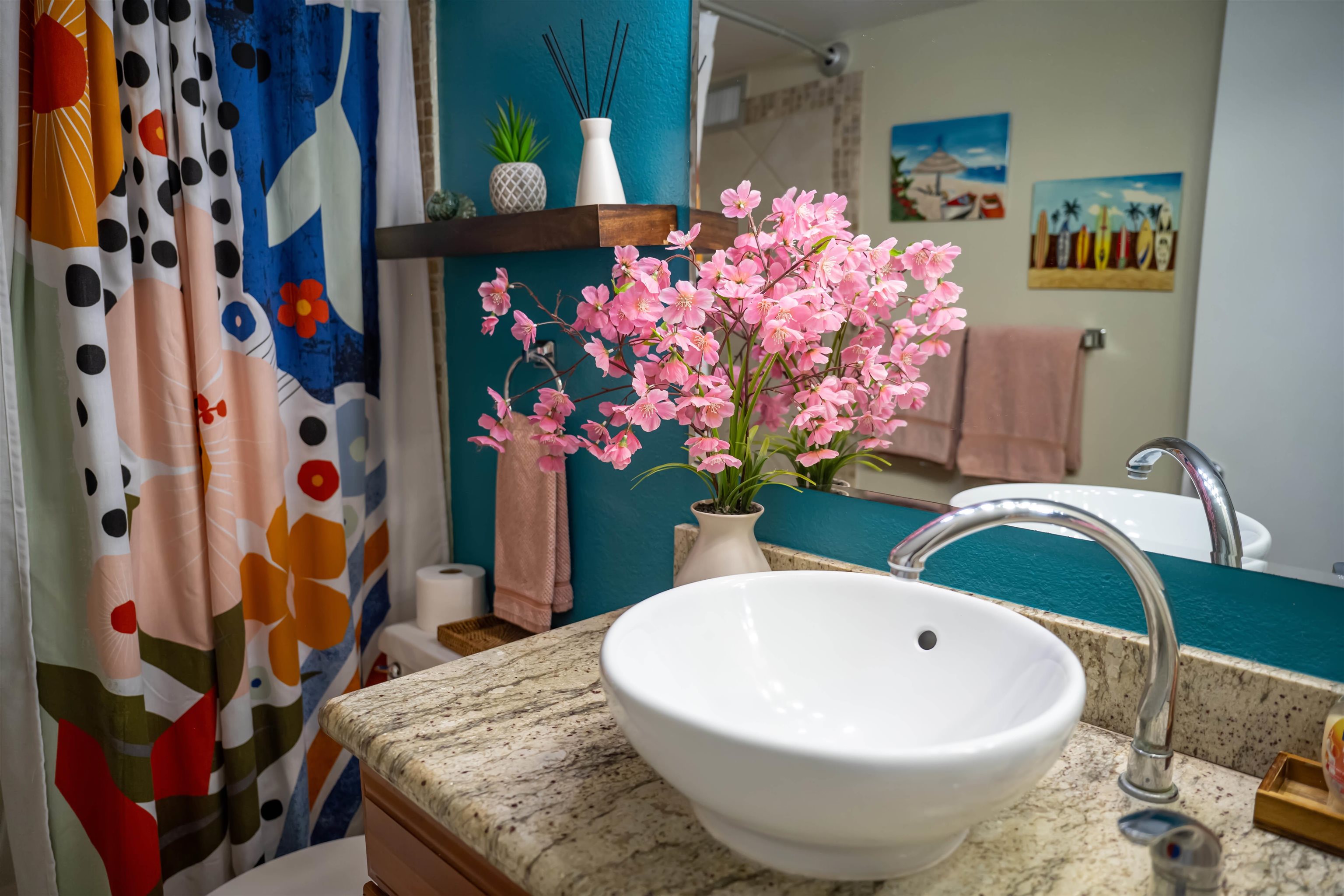 Bathroom vanity with a white vessel sink, granite countertop, turquoise wall, and colorful patterned shower curtain.