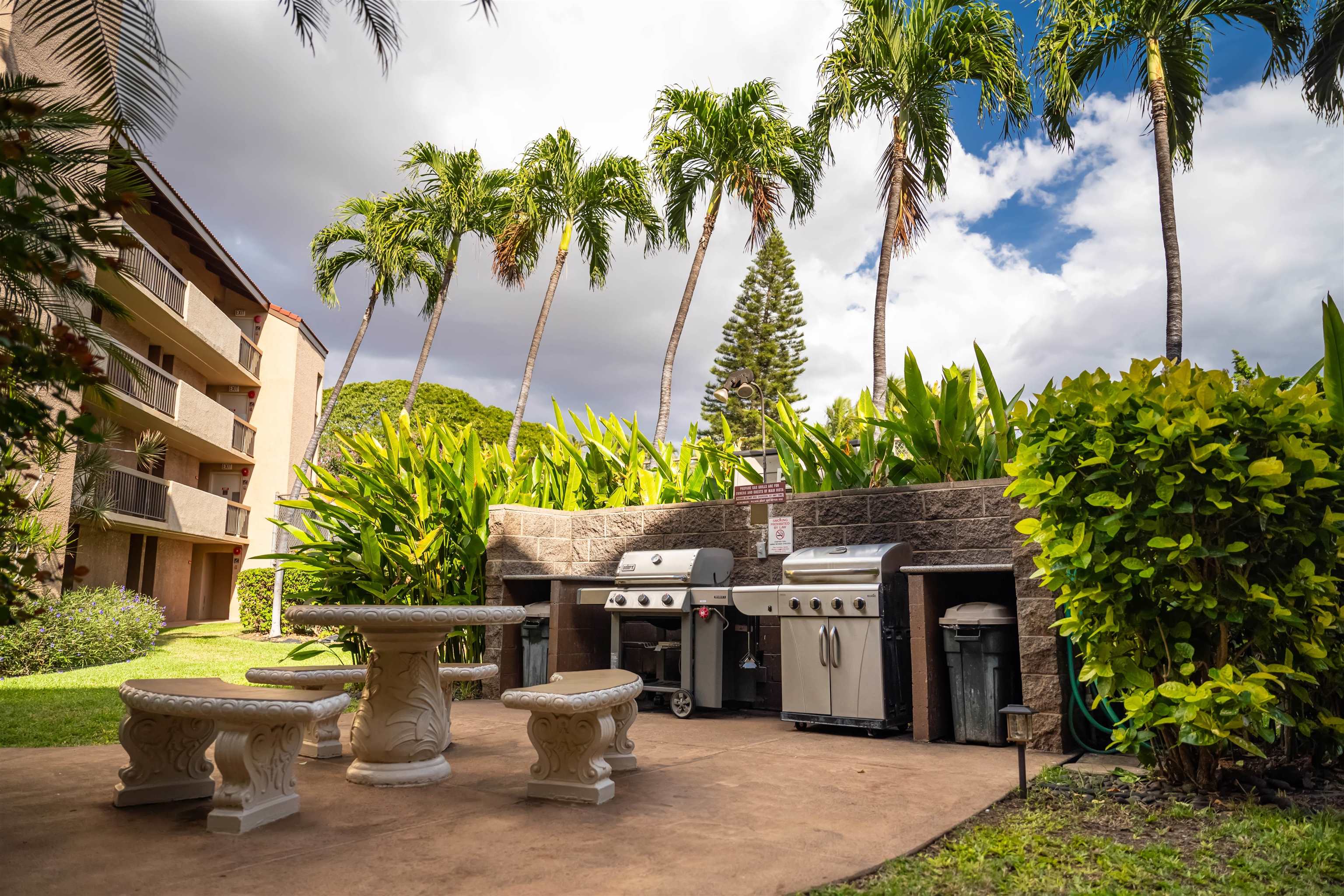 Condominium barbecue patio with stainless steel grills, stone tables and tropical landscaping.