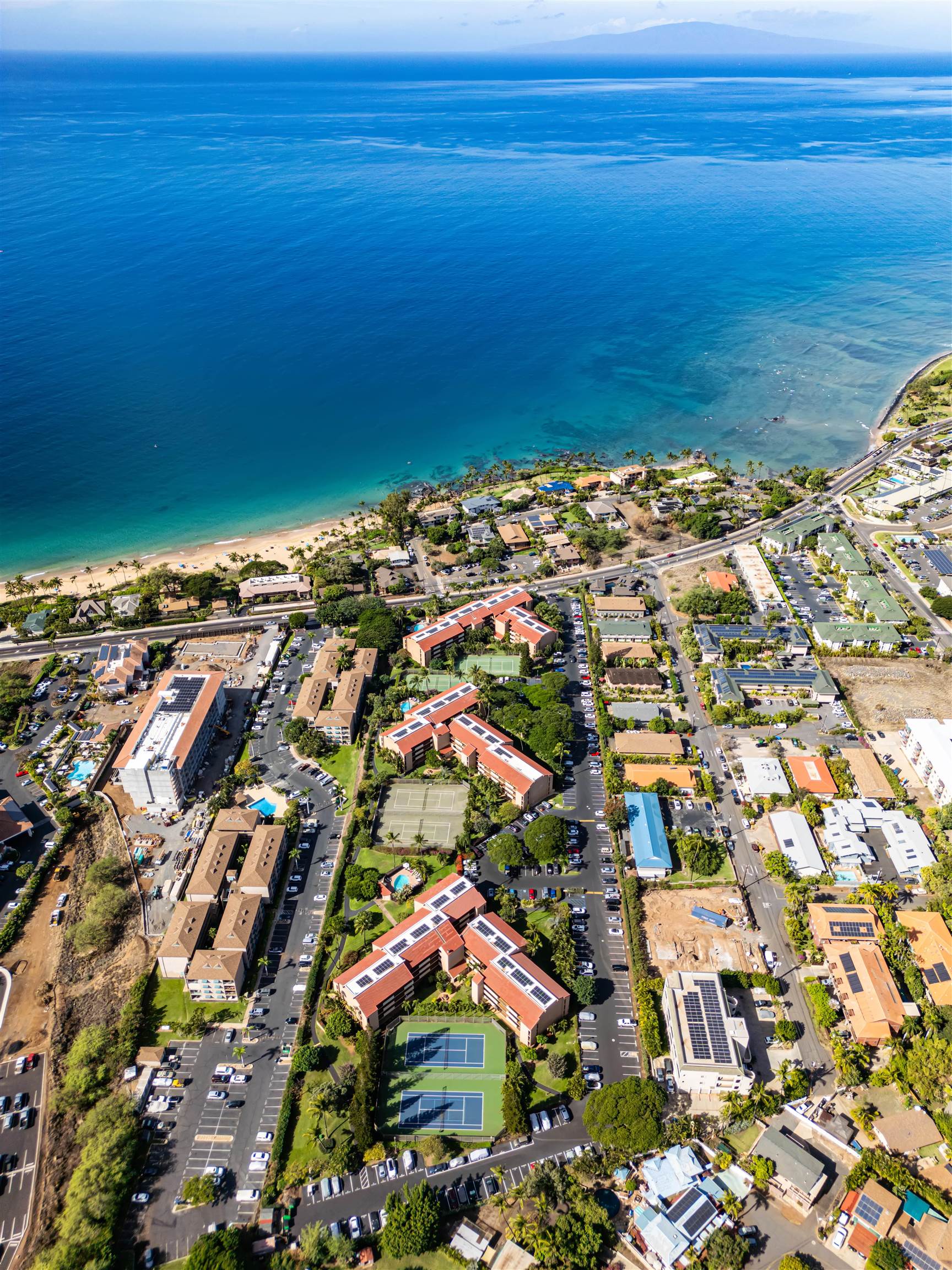 Aerial view of a Kihei coastal condominium complex beside the beach, with tennis courts and blue ocean.