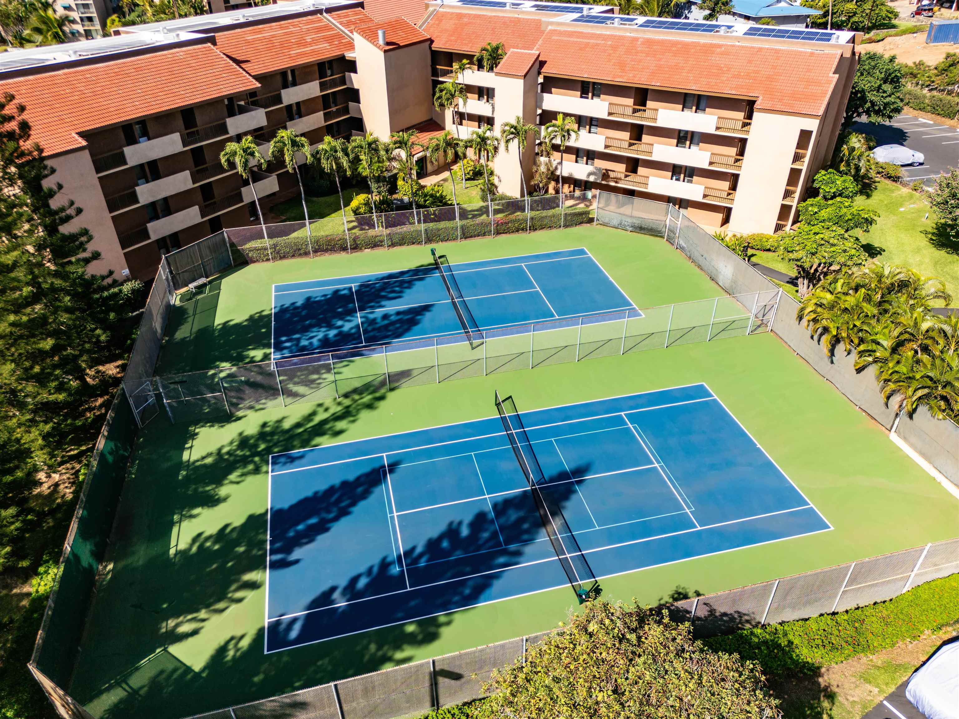 Two blue tennis courts beside a multi-story condominium complex, viewed from above.