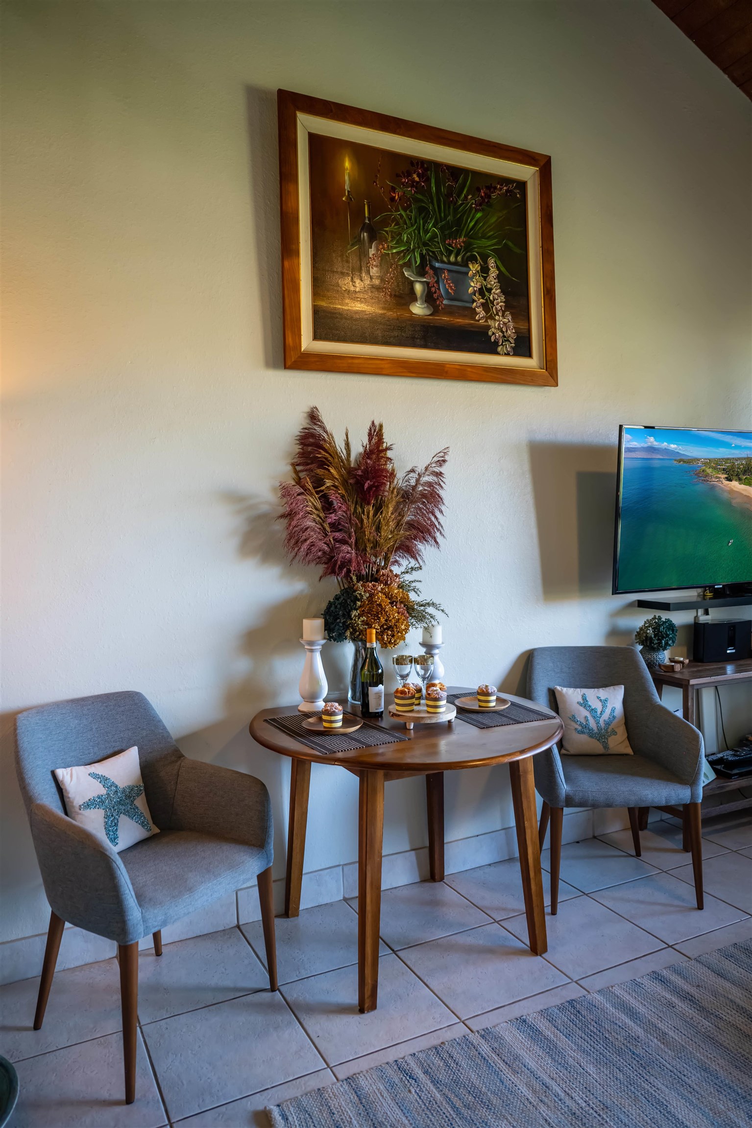 Furnished dining nook with a round table, two gray chairs, and a floral painting.