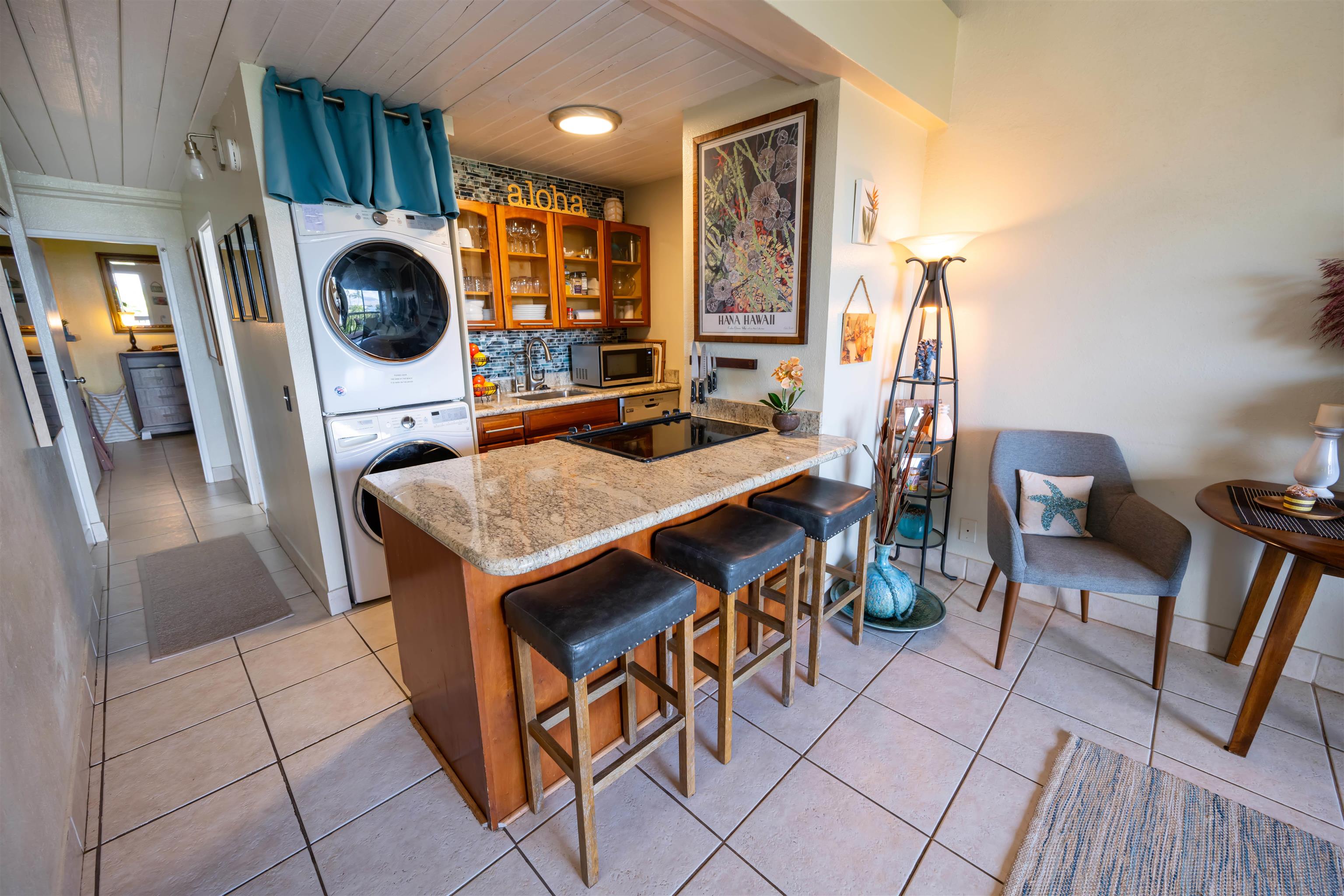 Kitchen with granite breakfast bar, wood cabinets, and stacked washer and dryer beside a sitting area.