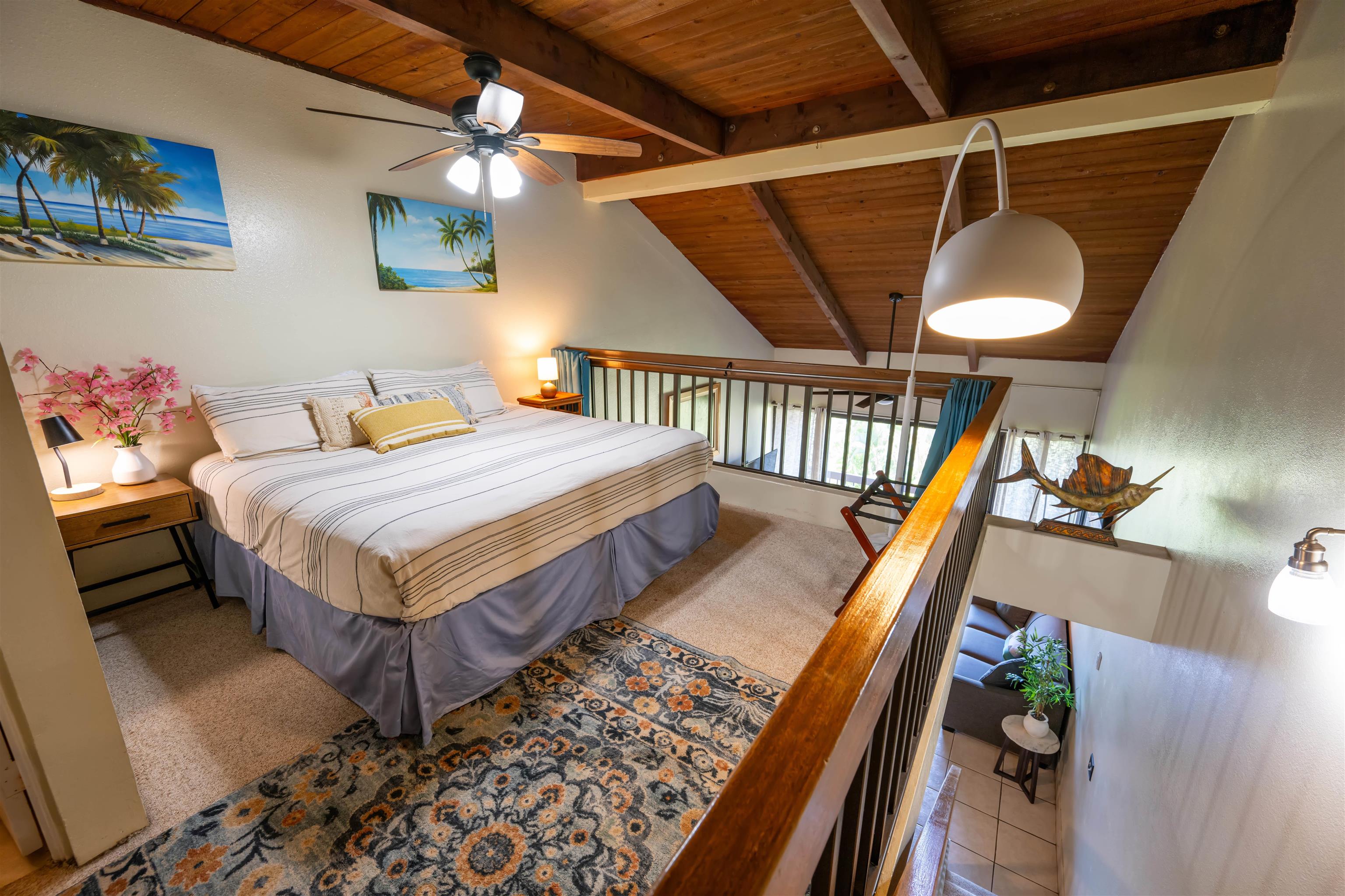 Loft bedroom with a striped bed beneath a vaulted wood ceiling, overlooking the living area.