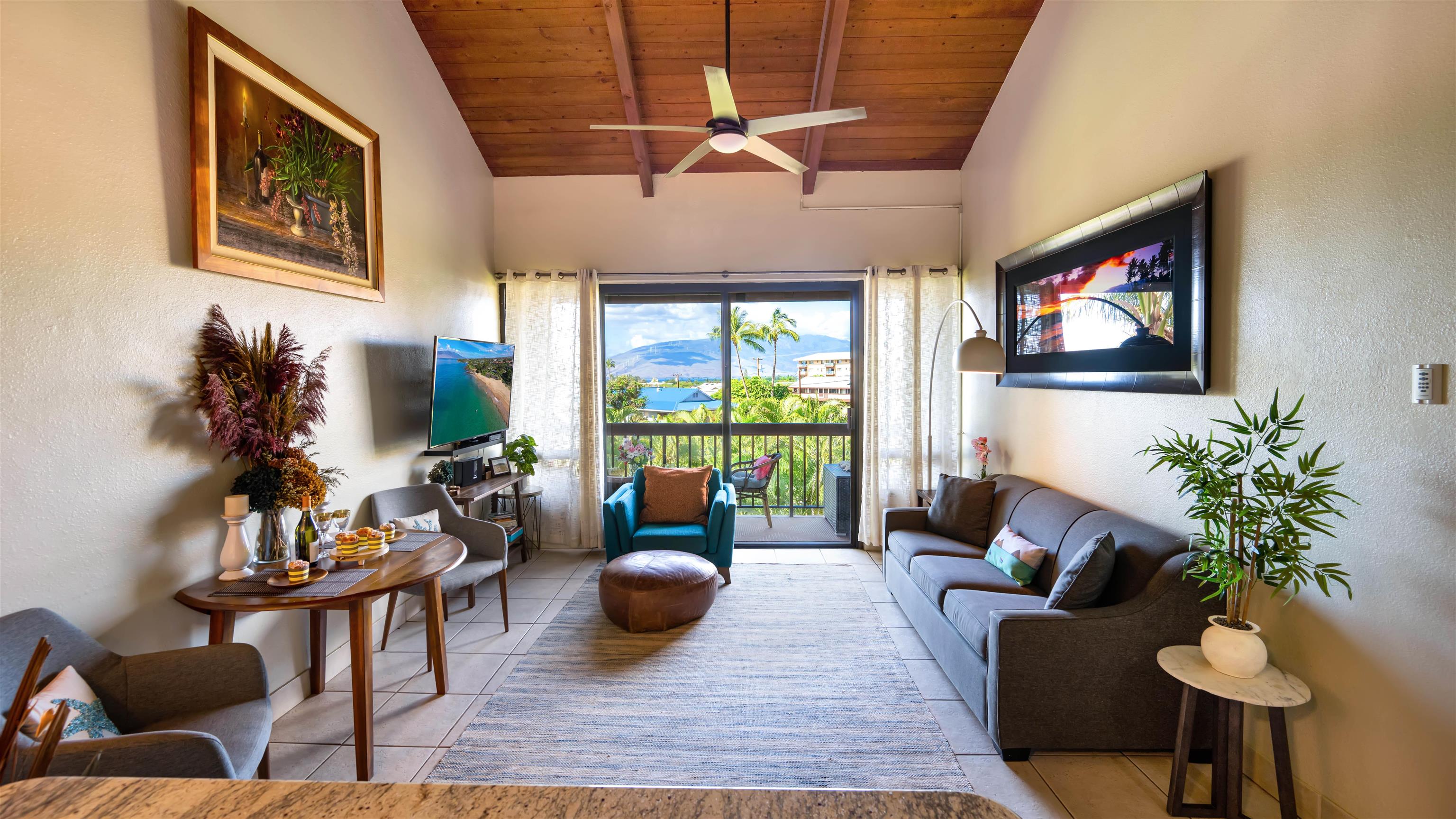 Furnished living room with a vaulted wood ceiling and balcony views of the ocean and mountains.