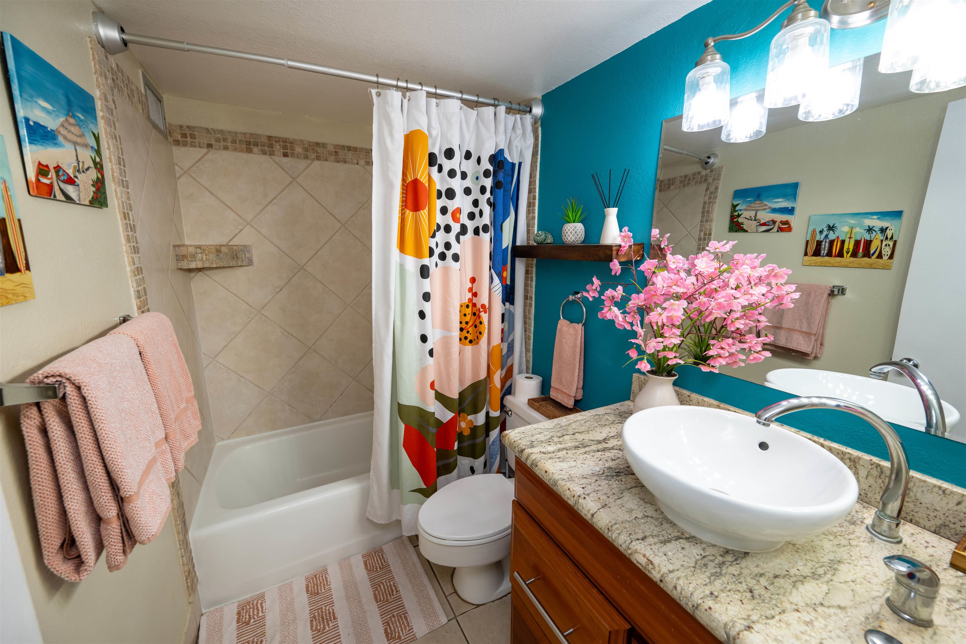 Bathroom with a tiled tub, colorful shower curtain, vessel sink, granite counter, and teal accent wall.